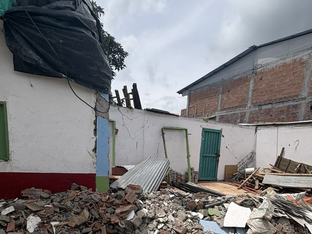 Muro blanco agrietado junto a una puerta, con escombro al pie